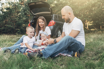 Young Couple with Their Little Children Having Picnic in Forest, Family Weekend Concept, Four People Enjoying Summer Time