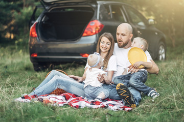 Young Couple with Their Little Children Having Picnic in Forest, Family Weekend Concept, Four People Enjoying Summer Time