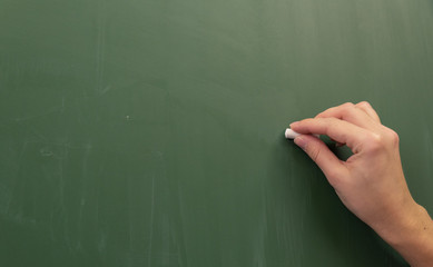 Female hand writing with chalk on empty green chalkboard.