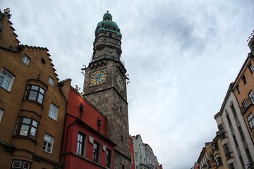 Closeup of an European church clock tower among colorful buildings on a cloudy sky