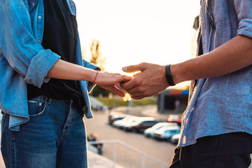 Closeup view of hands of lovely young couple dating during summer sunset. they wear jeans clothes. modern youth relationship
