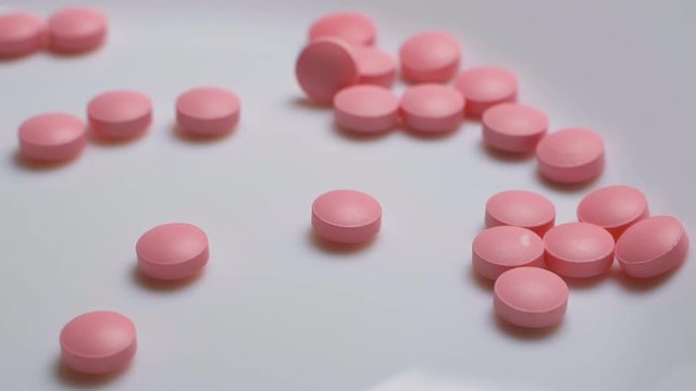Pink pills fall down on white background in slow motion