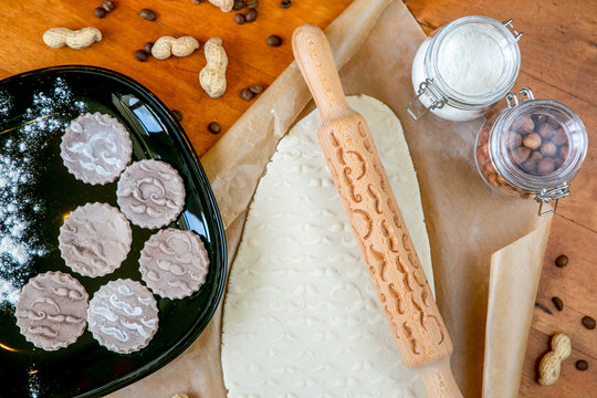 Rolling pin with a mustache pattern on a wooden decorated table covered with baked flour. Rolled dough with a pattern and cookie of various shapes. Biscuit cooking background, top view - Powered by Adobe
