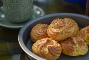 Choux cream or cream puffs in a tray fresh from the oven with coffee cup in the background.