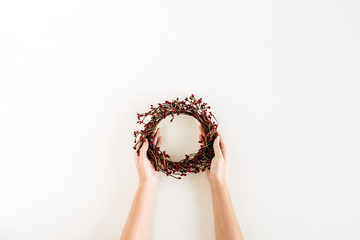 Wreath frame of red berries in female hands on white background. Flat lay, top view Christmas / New Year mockup composition.