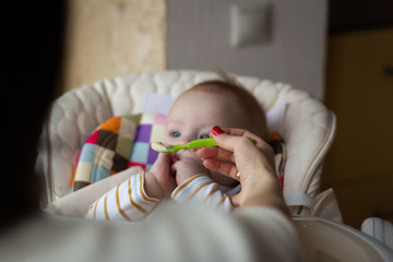 The first feeding of the baby from the spoon. Mom feeds baby homogenized chopped food with a spoon. child care.