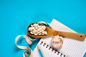 Sheet of Diet Plan and wooden spoon with a measuring tape on a blue background, diet, healthy lifestyle.