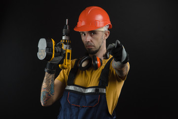Fototapeta premium a young man posing on a black background in a work uniform and a construction tool