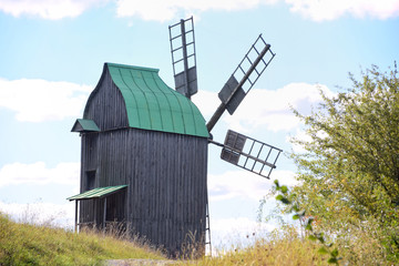 Fototapeta na wymiar old wooden windmill with green roof on blue sky background with autumn field on front