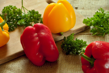 Fresh raw red and yellow bell pepper, paprika with green parsley on wooden board and rustic textile