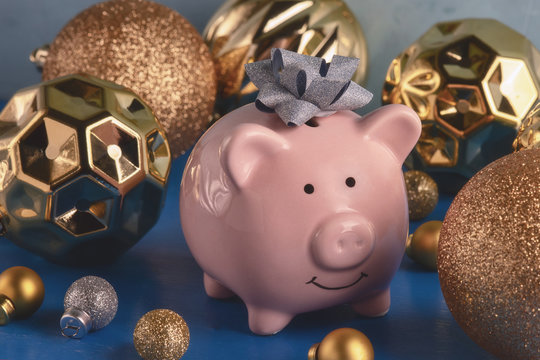 Little pink piggy bank with a bow on the head close-up. Nearby are a lot of gold and silver Christmas balls of various sizes. The symbol of the new year.