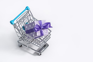  Gift box, in purple polka dot paper, decorated with ribbons and bows in shopping trolley .