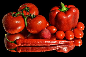 Red paprika, tomatoes, hot chili and radish on a black background with reflection, still life