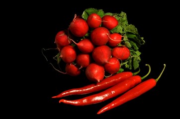 close up of a bunch of red radishes and three red hot chili peppers on a black background