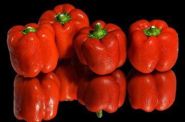 close up of four red bell paprikas on a black background with reflections