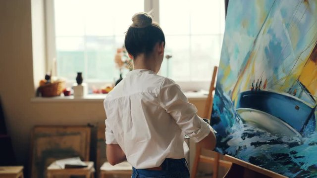 Professional female painter is working at picture using oil paints and palette-knife creating beautiful seascape on canvas. Painting technique and tools concept.