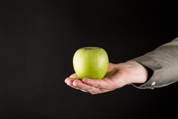 Hand giving a Green Apple. Man holding an apple. isolated on gradient black background, copy space.