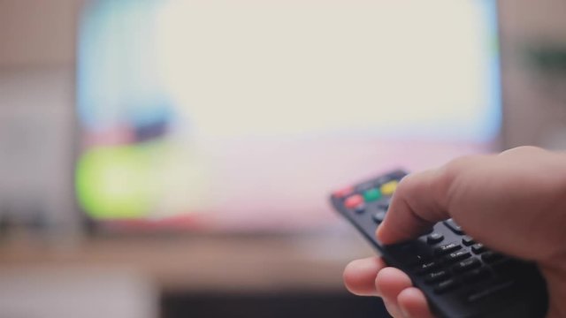 Male hand holding the TV remote control and changing television channels. Close-up and blurred background