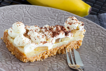 Piece of Banoffee pie with banana, chocolate, caramel and whipped cream. Selective focus.