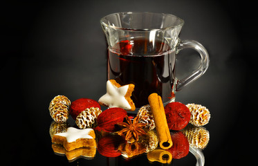 a glass of mulled wine with gingerbread cookies, cinnamon rolls and fir cones on a black background, still life
