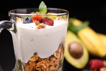 Yogurt with granola and fruits in glass on black granite stone table