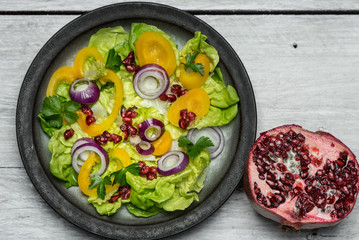 Healthy breakfast, fresh salad with the addition of purple onion and pomegranate seeds on white, wooden background