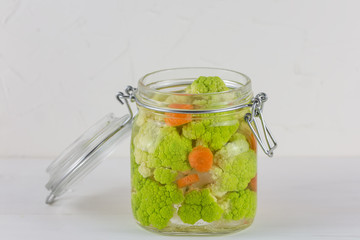 Fermented preserved vegetarian food concept. green cauliflower or broccoli sour glass jars on the white background
