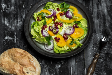 healthy diet, fresh salad with the addition of purple onion and pomegranate seeds on dark, wooden background