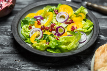 healthy diet, fresh salad with the addition of purple onion and pomegranate seeds on dark, wooden background