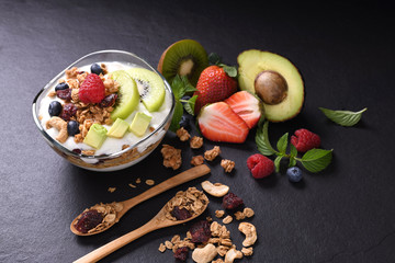 Yogurt with granola and fruits in glass on black granite stone table