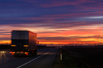 Obraz na płótnie Canvas A very colorful sunset and a moving (blurred) truck on an asphalt road