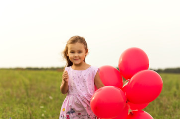 girl runs with red balloons in the summer in nature