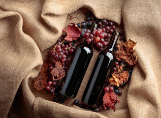 Red wine bottles and  grapes with dried up vine leaves.