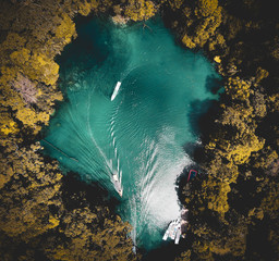 Beautiful overhead aerial photo of a crystal clear lake surrounded by trees with boats and boats' trails in Labuan Cermin, Indonesia.