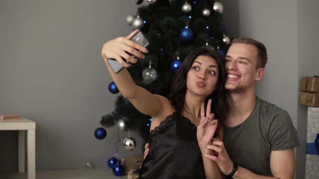 Capturing a happy moment, having fun together. Beautiful young loving couple bonding to each other and smiling while making selfie with Christmas Tree in the background. Loft interior room