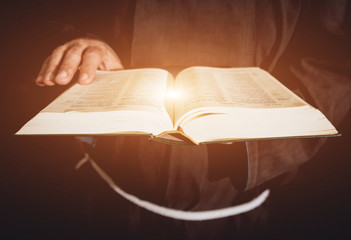 A monk in robes with holy bible in their hands praying in the church