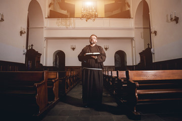 A monk in robes with holy bible in their hands praying in the church