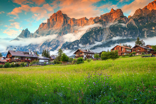 Spring alpine landscape with flowers, mountains and wooden houses, Italy