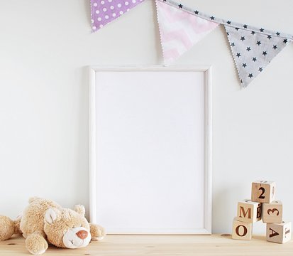 White frame mock up for photo, print art, text or lettering, with kids room decorations and toys. Blank frame on wooden table.