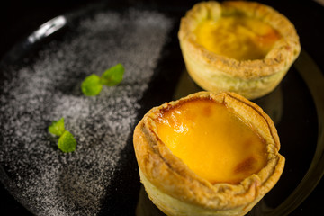 Egg tart, traditional Portuguese dessert on black plate, selective focus, copy space