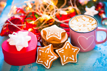 Cup of chocolate with marshmallow, gingerbread cookies, gifts and beautiful Christmas decorations with lights on the wooden background. Flat lay, top view, close up space for a text.