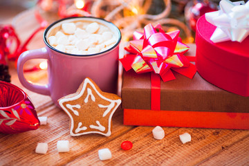 Cup of chocolate with marshmallow, gingerbread cookies, gifts and beautiful Christmas decorations with lights on the wooden background. Flat lay, top view, close up space for a text.