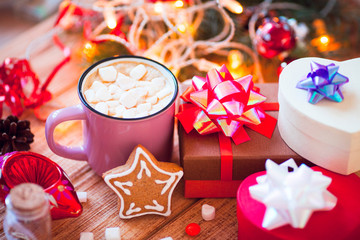 Cup of chocolate with marshmallow, gingerbread cookies, gifts and beautiful Christmas decorations with lights on the wooden background. Flat lay, top view, close up space for a text.