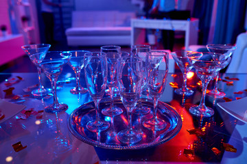 Set of various alcohol glasses composed on shiny table in confetti with neon lights 