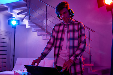 Young man in headphones playing music at DJ mixer in colorful lights on holiday party