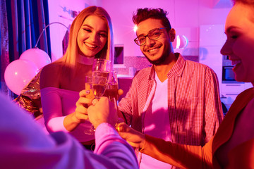 Group of young people celebrating New Year and clinking with glasses of champagne having house party 