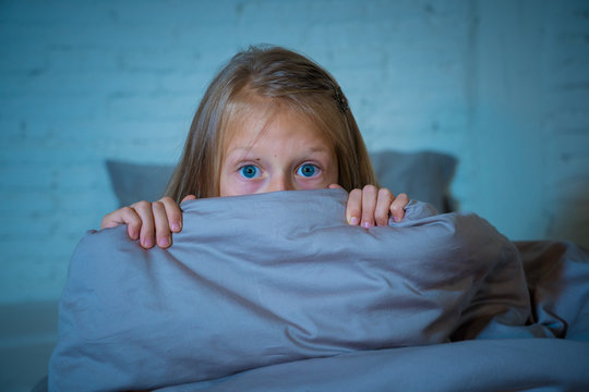 Sleepless cute girl in fear at night hiding behind the blanket afraid of dark and monsters