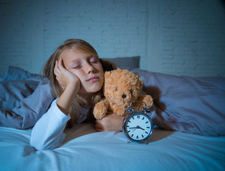 Little Girl in bed awake at night yawning and feeling restless showing clock she can not sleep © SB Arts Media