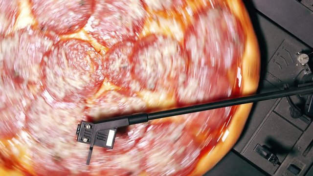 Pizza pepperoni spinning on turntable vinyl player as record. Concept of party with delicious fast food. Italian traditional cuisine with salami sausage and cheese. Top view.