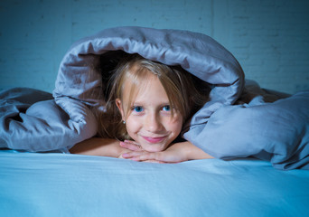 Beautiful cute little girl in bed under blanket looking joyful and happy at bedtime